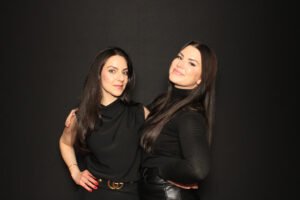 Two women smiling and posing in a photo booth against a black backdrop