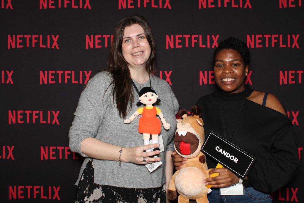 Guests posing with plush toys and a sign in front of a Netflix custom photo booth backdrop using photo booth props at a branded event activation.
