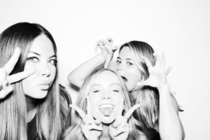 Three women striking playful poses in front of a studio-style photo booth backdrop, captured in high-quality black-and-white photo booth photos.