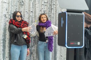 Two guests pose with money-themed photo booth props in front of a sparkling photo booth backdrop at a Vancity photo booth experience.