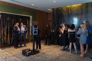 Guests line up for a sleek Vancity Photo Booth experience with glam lighting, posing in front of a sequin photo booth backdrop with playful photo booth props.