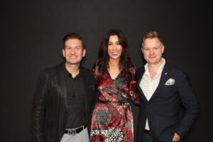 Three professionally dressed individuals smile for the camera against a solid black backdrop, creating a sleek and sophisticated group portrait.