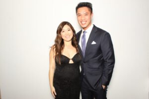 Couple dressed in formal attire smiling in front of a white photo booth backdrop at an event in Vancouver.