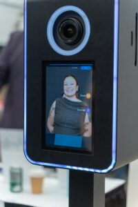 Close-up of an AI-powered photo booth touchscreen displaying a preview of a professionally lit headshot of a smiling woman, taken at a public event in Vancouver.