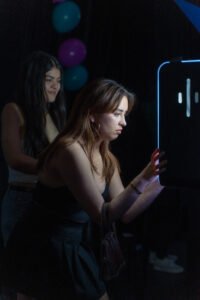 Woman interacts with an open-air photo booth equipped with instant sharing and photo printouts, while another guest waits behind her.