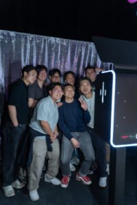 A group of students pose together in front of a silver sequin backdrop at a late-night event using a modern photo booth rental in Vancouver.