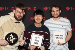 Three smiling guests pose with playful signs in front of a Netflix-branded backdrop during a corporate event in Vancouver, captured inside a Vancity photo booth rental.