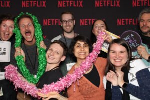 A lively group of Netflix employees pose together in front of a branded backdrop at a Vancouver event, smiling and holding colorful props inside a Vancity photo booth rental setup.