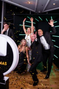 Group of well-dressed adults celebrating in a 360 photo booth with confetti, lights, and high energy at a downtown Vancouver event.